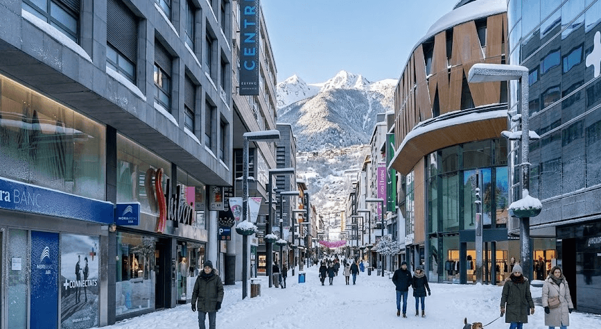 Una calle comercial cubierta de nieve en una ciudad de montaña, con peatones caminando junto a edificios modernos y picos nevados distantes bajo un cielo despejado.