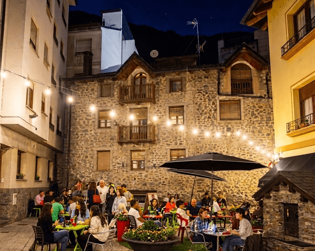 Nucli antic d'Andorra amb taules, para-sols i llums càlides en una plaça del poble.