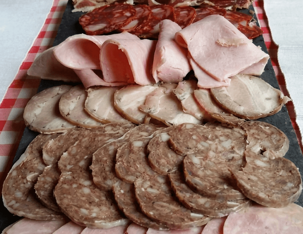 Un primer pla d'una safata plena de diversos embotits i carns fredes tallades a rodanxes, incloent pernil dolç, fuet i xoriço, disposats en una taula fosca.