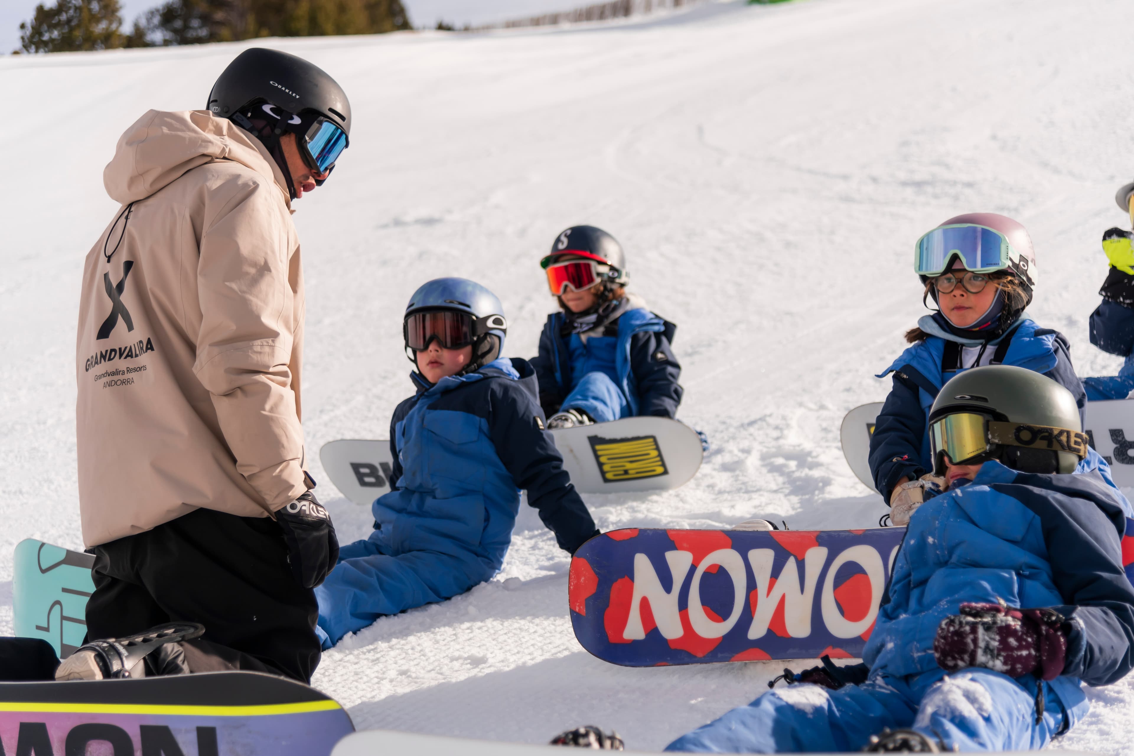 Instructor de Grandvalira dando una clase de snowboard a cuatro niños sentados en la nieve en Andorra.