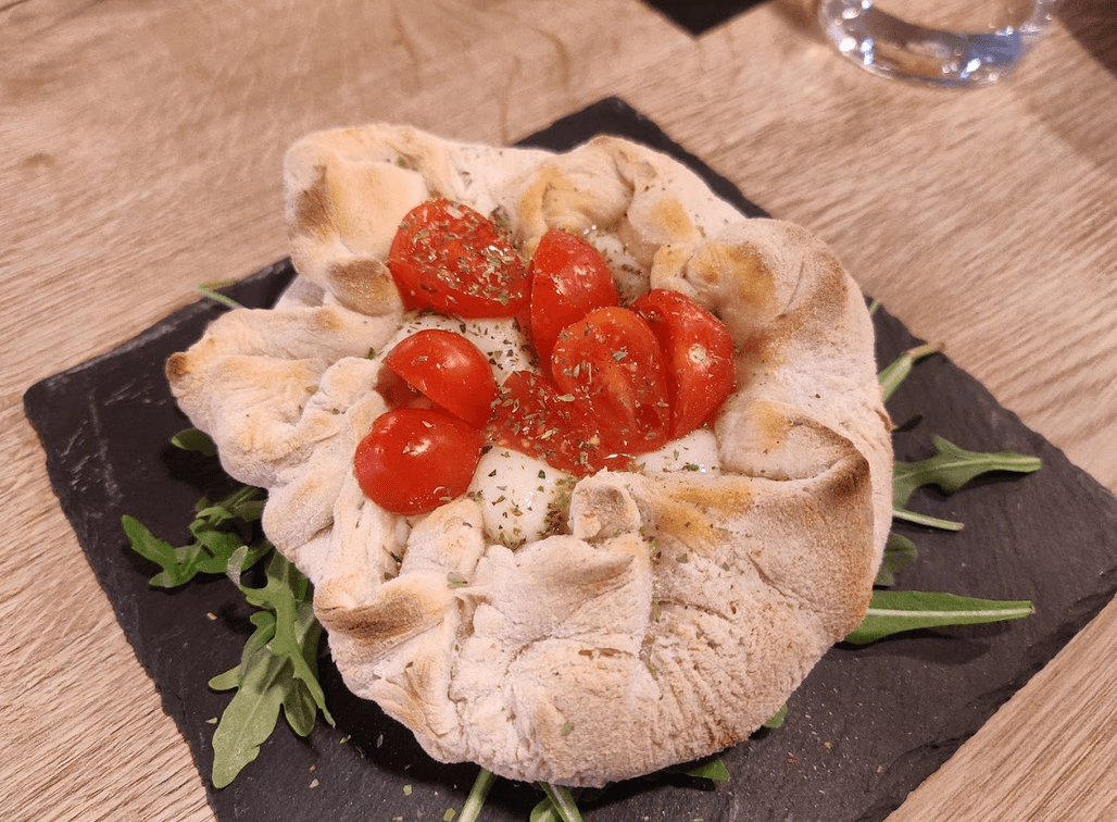 Plato de Una especie de focaccia con queso dentro y con tomates cherry encima