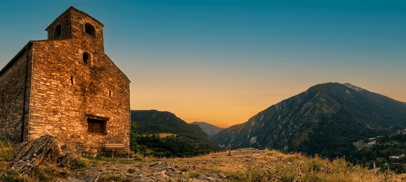 Una antigua ermita de piedra con campanario se alza en una colina rocosa, con vistas a un vasto valle montañoso bañado por la cálida luz del atardecer.