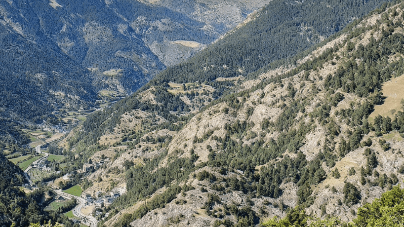 Una vista aérea de un profundo valle de montaña, con una carretera serpenteante, un río y un pequeño pueblo anidado entre laderas empinadas y boscosas y terreno rocoso.