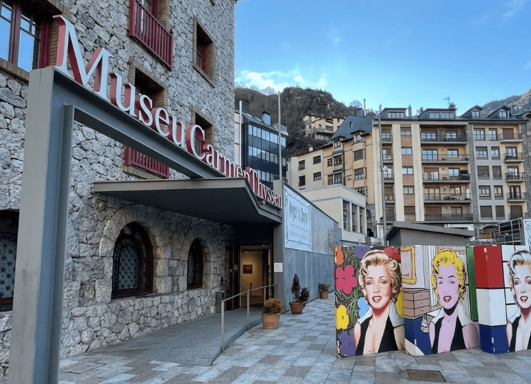 La fachada de piedra del edificio del Museo Carmen Thyssen con un letrero rojo, que muestra una rampa que conduce a la entrada y paneles de arte pop de Marilyn Monroe en el exterior.