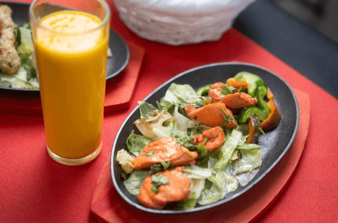 Ensalada de verduras con un zumo de naranja al lado sobre un mantel rojo del restaurante Namaste de Andorra