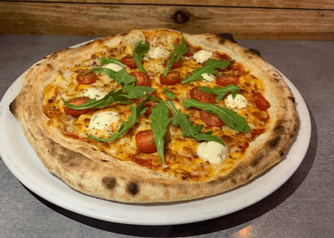 Una pizza acabada de fer amb formatge fos, tomàquets cherry, ruca fresca i trossos de mozzarella en un plat blanc.