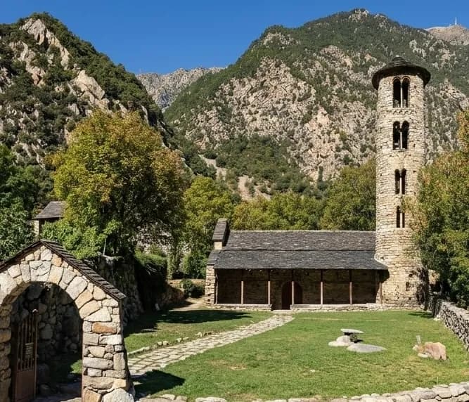 Una església de pedra amb un campanar rodó i una teulada fosca s'alça sobre una gespa verda, envoltada d'arbres i muntanyes sota un cel blau clar. Un arc de pedra es troba en primer pla.