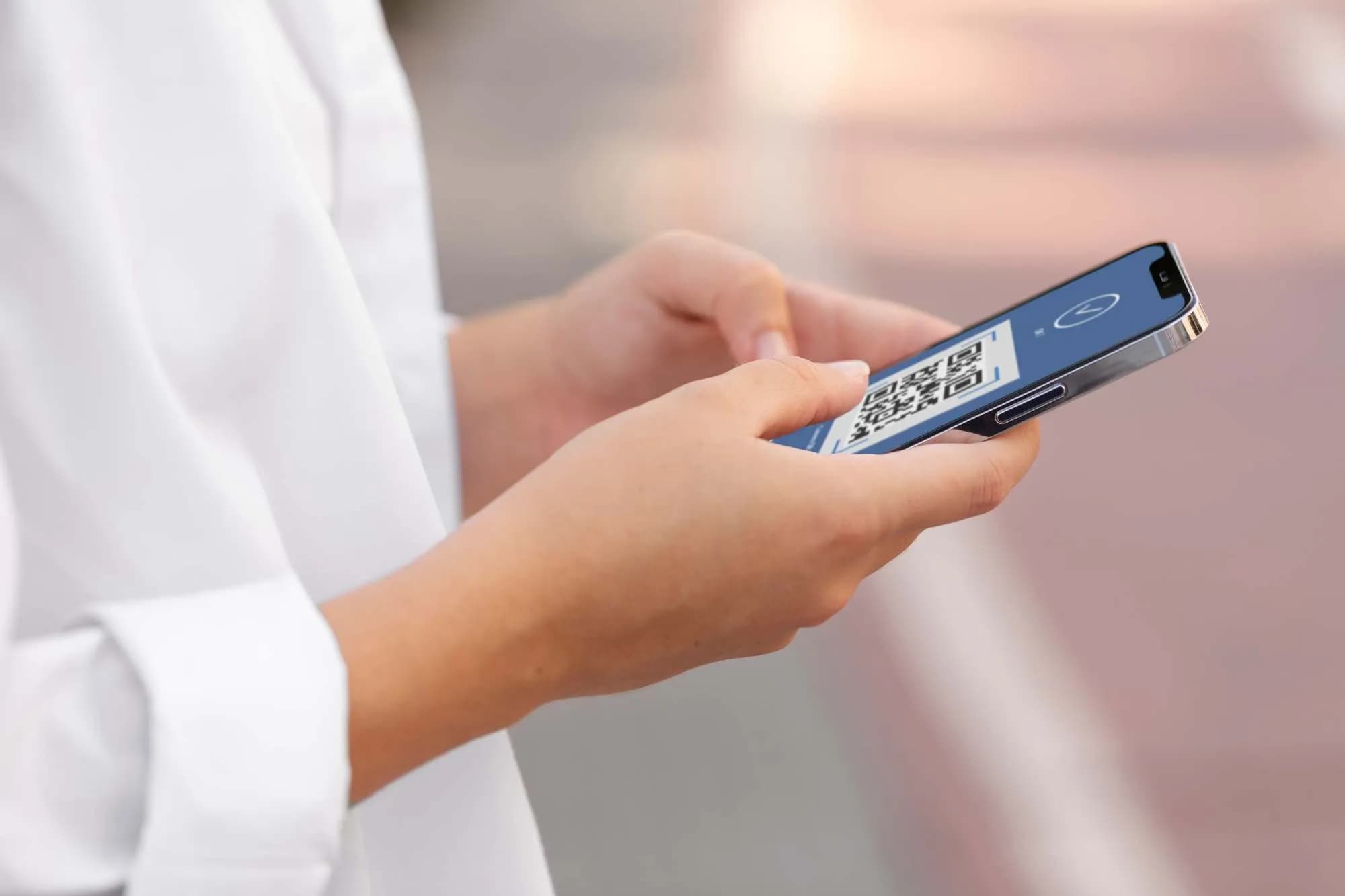 Une personne tient un smartphone affichant un code QR sur son écran. Ses doigts sont positionnés comme s'ils interagissaient avec le téléphone.