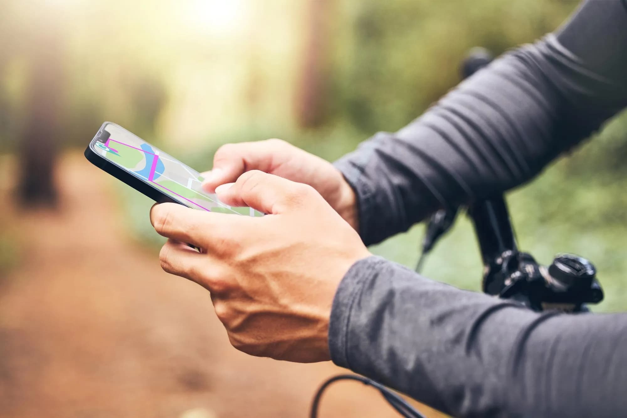 Gros plan des mains d'une personne tenant un smartphone affichant une application de carte, avec un guidon de vélo au premier plan et un chemin extérieur flou.