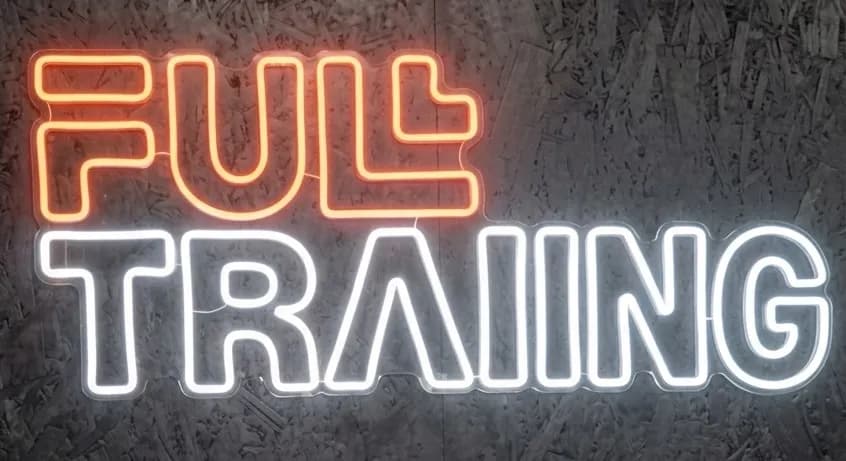 Rètol de neó en una paret fosca i texturada que mostra la paraula "FULL" en taronja i "TRAINING" en blanc.