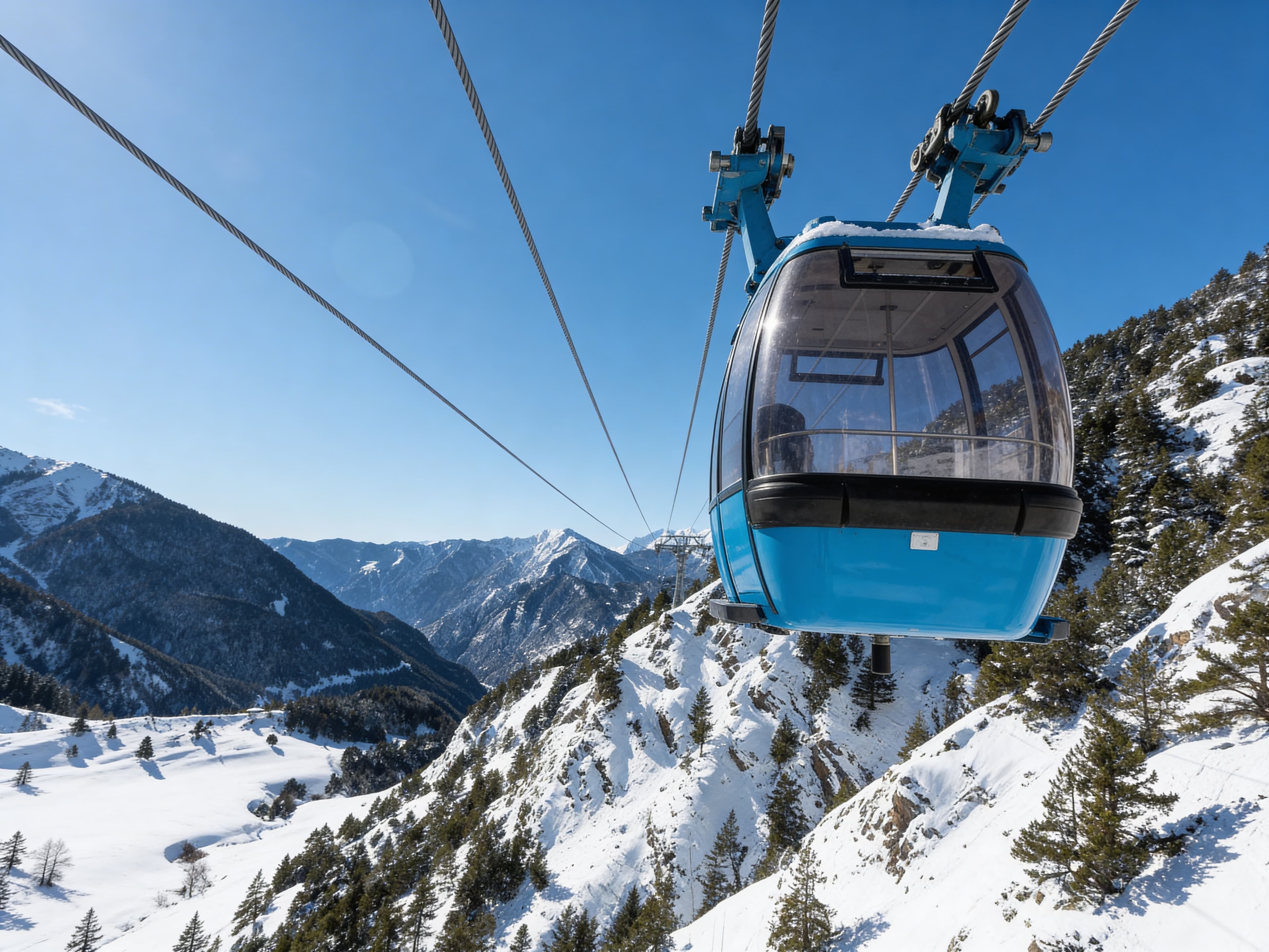 Una cabina de telecabina azul asciende sobre un paisaje montañoso cubierto de nieve bajo un cielo azul claro. Pinos salpican las laderas nevadas y se ven picos distantes.