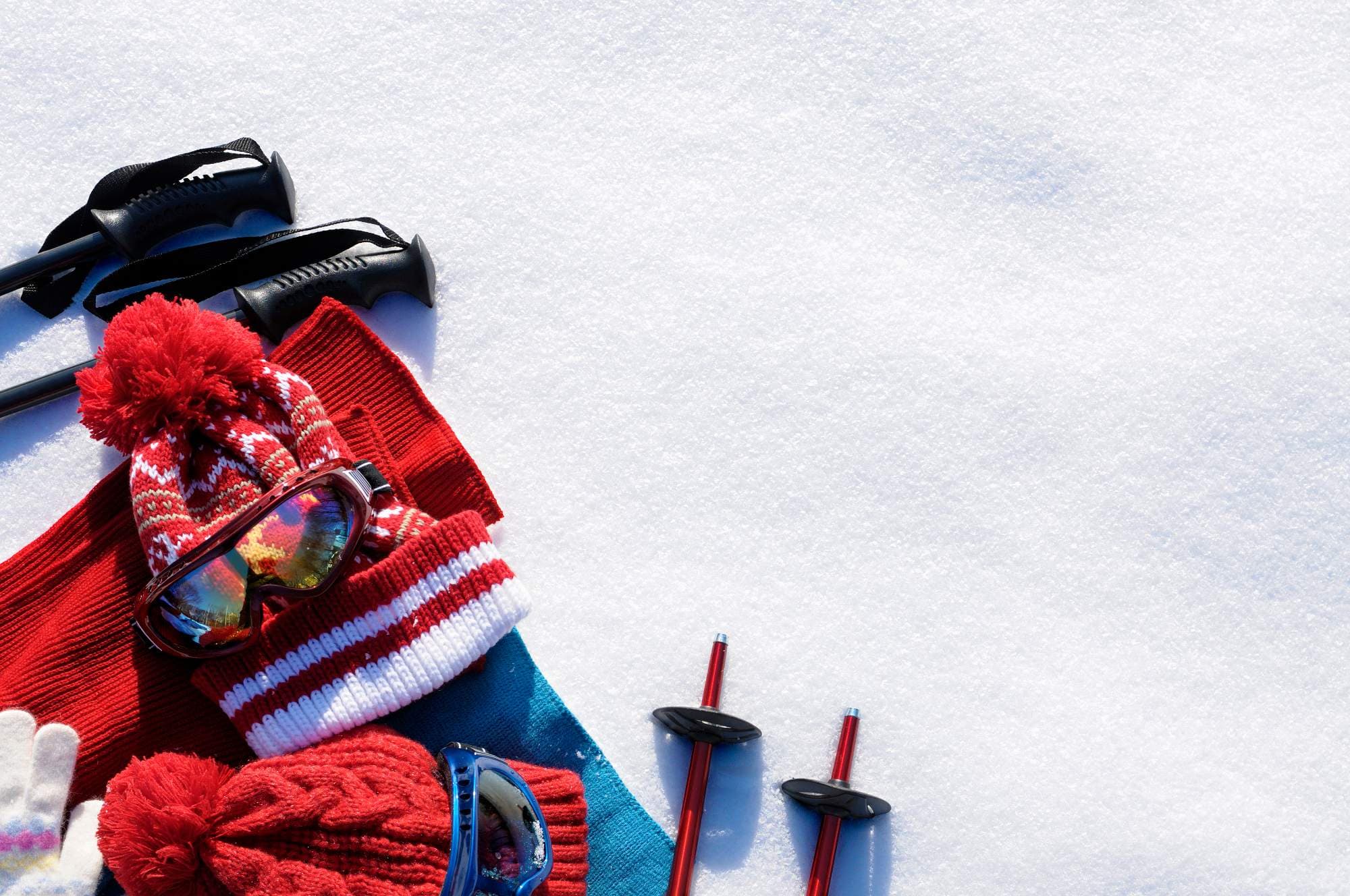 Accesorios de deportes de invierno como gorros de punto rojos, gafas de esquí, guantes y bastones de esquí están dispuestos sobre un lecho de nieve fresca.