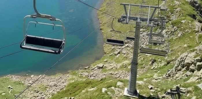 Un telecadira amb seients buits penja sobre un llac blau clar i una vessant rocosa i verda. Una torre del telecadira es troba a la dreta.