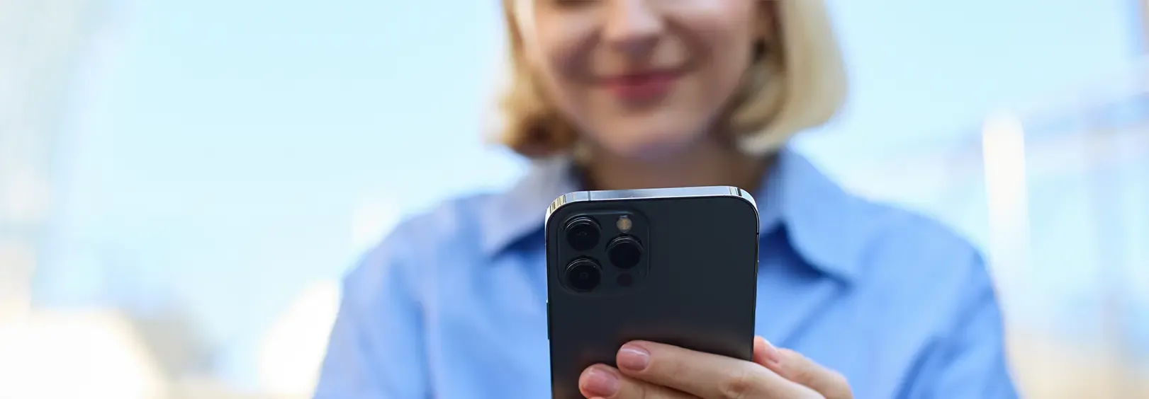 Una persona sostiene un smartphone, con su sistema de triple cámara prominentemente visible. El rostro de la persona está borroso en el fondo, sugiriendo que está mirando el teléfono.